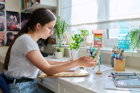 Teenage creative girl artist drawing with a pencil, sitting at the table at home