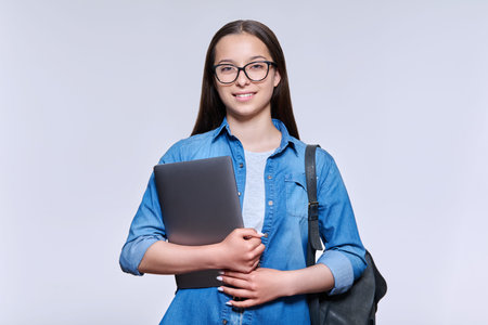 Teenage female student with backpack laptop looking at camera on light background