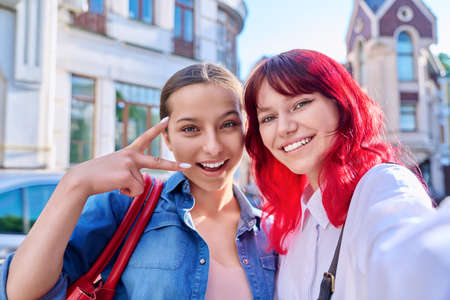 Two happy teenage females taking selfie portrait together, on city streetの写真素材