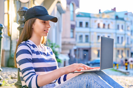 Teenage student girl using laptop outdoor, urban background