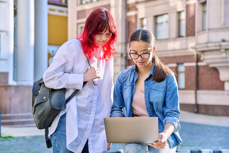Two teenage female students using outdoor laptop, city street backgroundの写真素材