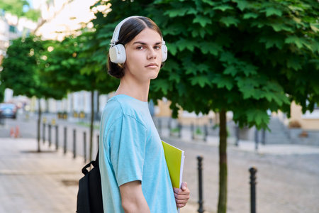 Smiling teenage male student with textbooks looking at camera outdoor