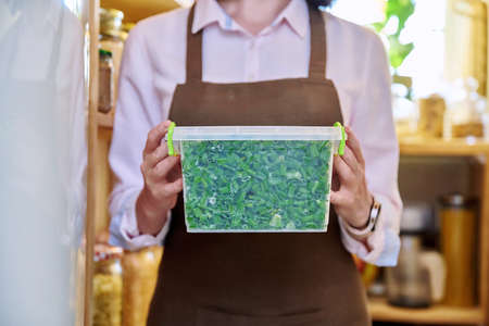 Woman with container of frozen green onions, in kitchen in pantry near freezer.の写真素材