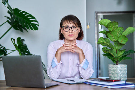 Middle aged woman looking at camera sitting at her desk with laptop