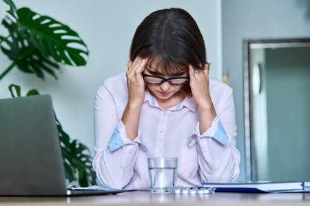 Tired middle-aged woman suffering from headache at workplace with laptop