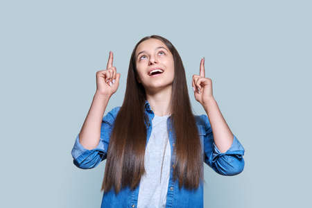 Teenage girl pointing fingers up at the place for text, on gray backgroundの写真素材