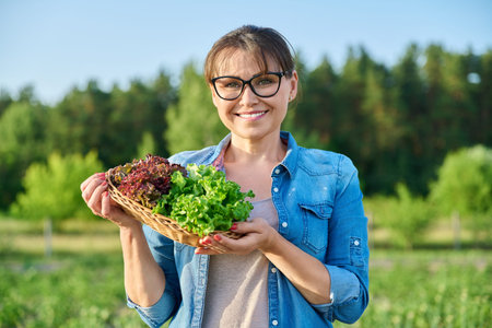 Portrait of smiling mature woman with harvest of red and green lettuce leaves in wicker bowl.