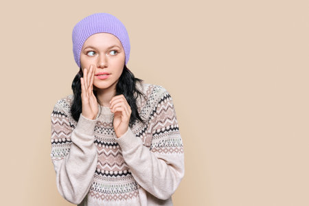 Teen girl in winter sweater hat telling secret rumors, on brown backgroundの写真素材
