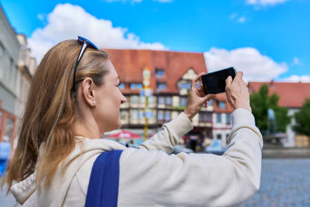 Woman tourist tourist taking photo in an old european city, in front of historical buildingの写真素材