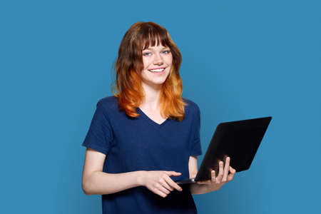 Red-haired teenage girl with laptop on blue background.の写真素材