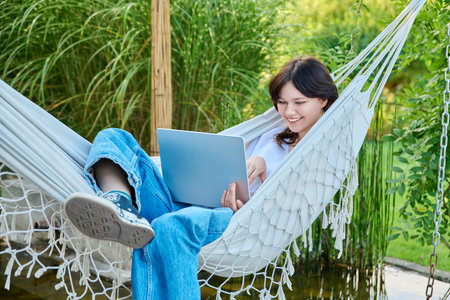 Teenage girl relaxing in hammock using laptop for leisure studyの写真素材