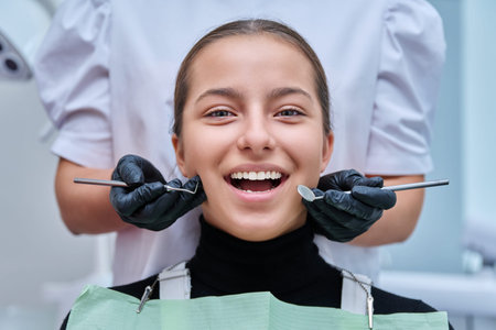 Teenage girl in dental chair with hands of dentist with toolsの写真素材