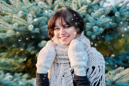 Portrait of young woman in knitted scarf mittens in winter, near Christmas tree
