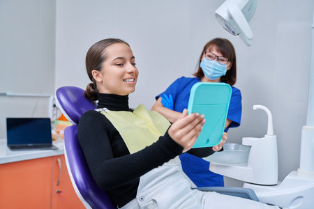 Happy female with mirror sitting in dentist chair looking at healthy teethの写真素材