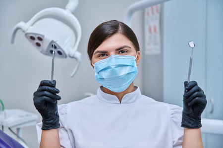 Portrait of female dentist in mask with instruments for examining teethの写真素材