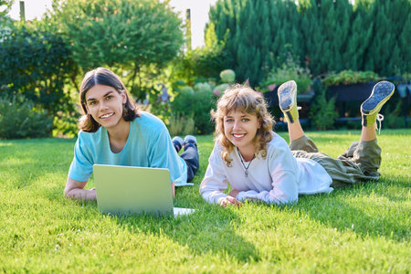 Two teenage friends of students lying on grass with laptop, in backyardの写真素材