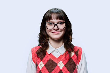 Portrait of young smiling female student looking at camera on light background
