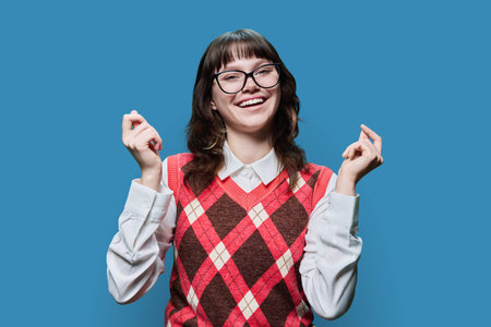 Young female student in glasses having fun on blue background