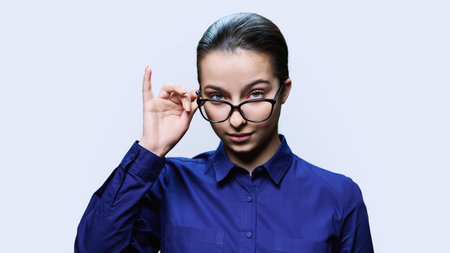 Teenage girl student holding glasses looking at camera on white background