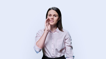 Young woman telling secret, holding her hands near her lips, on white background