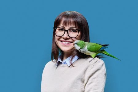 Middle aged woman with green Quaker parrot on her shoulder, on blue backgroundの写真素材