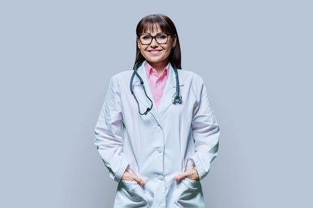 Portrait of middle-aged woman doctor in white coat on gray studio backgroundの写真素材