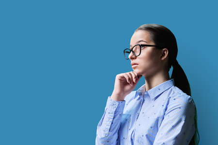 Portrait of a high school student girl, copyspace blue background. Profile view, confident serious female in glasses looking awayの写真素材