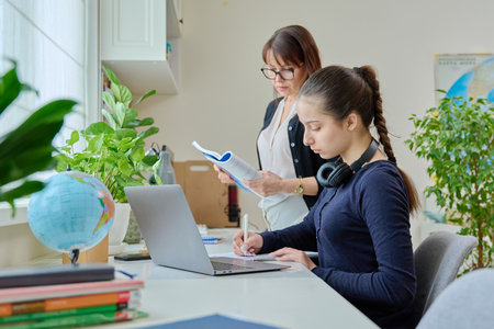 Teenage girl studying, female teacher with textbook helps tells teachesの写真素材