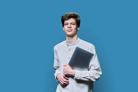 Portrait of young college student guy with laptop on blue backgroundの写真素材