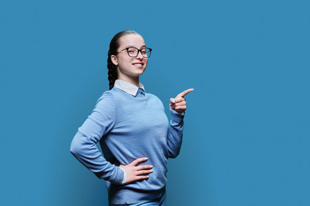 Teenage girl pointing with finger at empty space for text, blue studio background.の写真素材