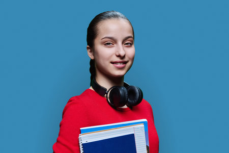 Portrait of smiling high school student girl with textbooks on blue backgroundの写真素材