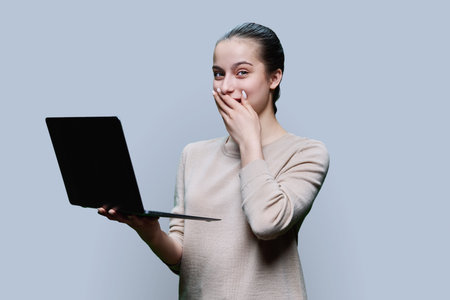 Surprised teen girl using laptop on grey studio backgroundの写真素材