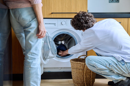 Young guy at home using washing machine with basket of dirty thingsの写真素材