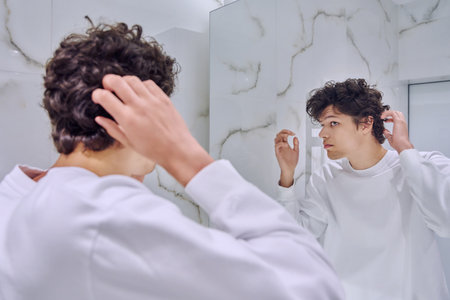 Young male looking at himself in bathroom mirror, touching curly hairstyleの写真素材