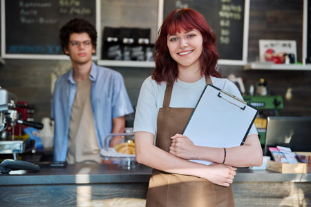Portrait of young female waitress in front of counter in coffee shopの写真素材