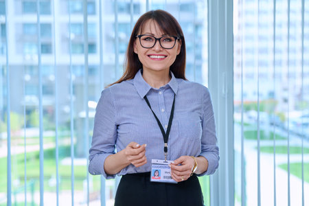 Middle aged woman with educational center badge, in office near windowの写真素材