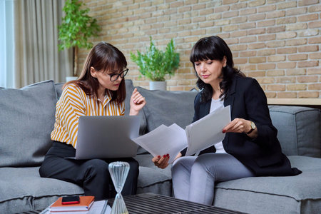 Two business mature women sitting on couch in office, talking, discussing work