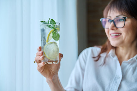 Cool drink mineral water with ice lemon mint leaves in womans handの写真素材