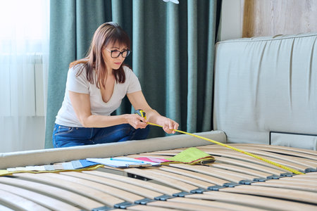 Woman textile designer with tape measure measuring size of bed in bedroomの写真素材