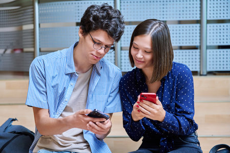 Friends college students guy and girl with smartphones inside educational building