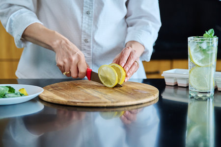 Closeup of a womans hands preparing cold cocktail with lemon, mint leaves and iceの写真素材