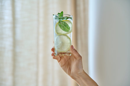 Cool drink mineral water with ice lemon mint leaves in womans hand