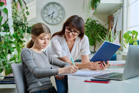 Mother helping preteen daughter to study, looking at laptop at homeの写真素材