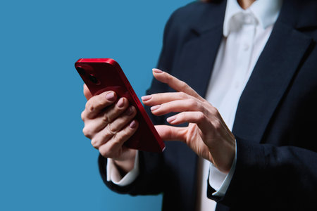 Closeup of business womans hands using smartphone, on blue background