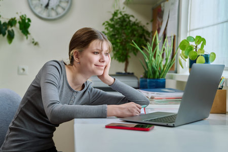Teenage girl studying online at home, using laptop, having video lesson