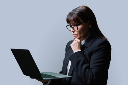 Serious mature woman using laptop, on grey backgroundの写真素材