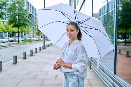 Young teenage female on summer cloudy day under white umbrella on city streetの写真素材
