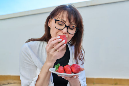 Middle aged woman eating strawberries with pleasureの写真素材