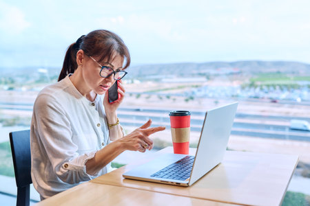 Middle aged woman in airport cafe working with laptop computerの写真素材