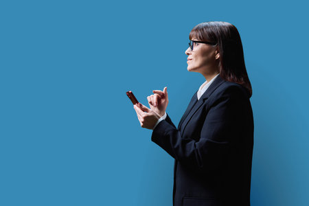 Mature business woman with smartphone, profile view on blue backgroundの写真素材